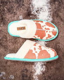 Pair of cow print slippers with turquoise trim on a fur surface