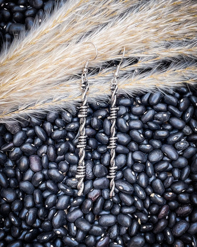 Silver earrings on a bed of black beans with a straw background