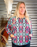 A woman wearing a long sleeve pullover with an aztec pattern in pink, white, black, and turquoise colors.