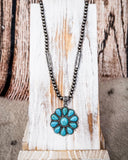 The Lola Flower Pendant Fashion Necklace displayed on a wood plank.