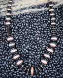 Brushed copper faux Navajo pearl necklace displayed on natural black beans and dried grass.