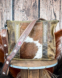 Handbag with cowhide leather and decorative strap on a wooden stool against a wooden background