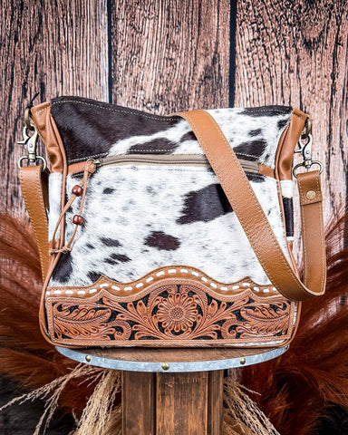 Cowhide leather handbag with brown leather accents on a wooden stand against a wooden background