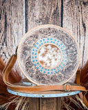 Round leather bag with intricate patterns and a cowhide patch on a wooden background