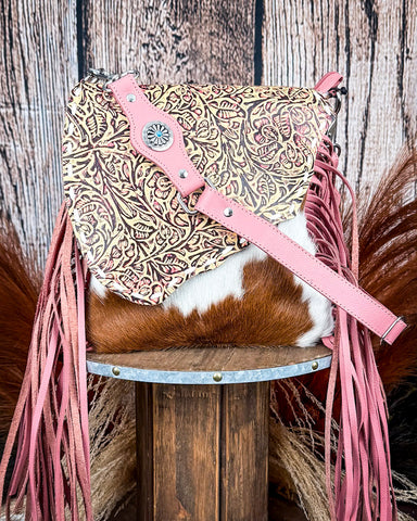 Pink leather bag with floral pattern and fringe on a wooden stool