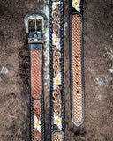 Decorative leather belt with floral and woven patterns on a textured brown background