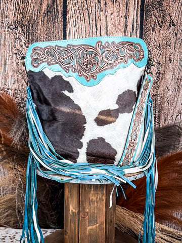 Front view of the Pony Trail Fringed Hand-Tooled Bag on a wood table with a wood back drop.