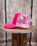 Side view of the Country Club Pink Cow Print Trucker Cap displayed on a wood table, wood backdrop.