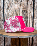 Side view of the Country Club Pink Cow Print Trucker Cap displayed on a wood table, wood backdrop.