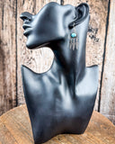 The Abey Genuine Turquoise Fringe Earrings on a mannequin, sitting on a wood table, wood backdrop.