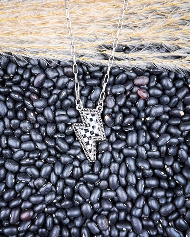 The Checkered Lightning Pendant Fashion Necklace displayed on pebble and wheat background.