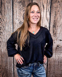 The Hadley Top in black styled and modeled on women in front of wood background.