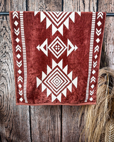 The Myna Mesa Towel hanging from a metal rod with wheat behind it in a wood background.