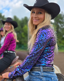 Woman in a colorful shirt and black cowboy hat on a horse, with another person in the background.