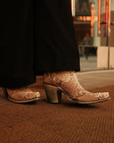 Person wearing python cowboy boots on a textured surface with a blurred background
