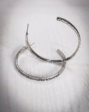 The Folk Tooled Hoop Fashion Earrings sitting on a wood table.