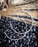The Folk Tooled Hoop Fashion Earrings displayed on beans and wheat with a cow skull in the corner.