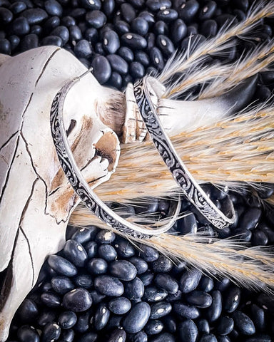 The Folk Tooled Hoop Fashion Earrings on a cow skull horn with wheat, displayed on beans.
