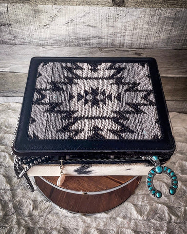 The Myra Bag - Mausoleum Jewelry Box sitting on a wooden wire wheel with jewelry hanging out of the opening. the table is on gray carpet.