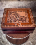 The Statuesque Jewelry Box closed showing the floral design on the top. The box is sitting on a wooden table on a gray carpet.