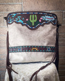 A hand-tooled cowhide purse with a floral pattern, featuring a cactus and fringe design in multicolor on a tooled leather surface.
