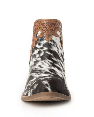 A single women's western ankle boot shown from the front on a white background. The boot features a black and white cowhide patterned lower section, a brown leather shaft with ornate cutout western embroidery, and a light brown sole.