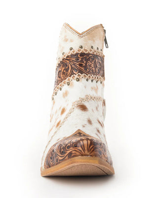 A single western-style ankle boot shown from the front on a white background. The boot features a white and tan cowhide pattern with dark brown tooled leather detailing around the collar, vamp, and quarter panels, and a small silver zipper at the top.