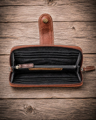 An open brown leather zip-around wallet with multiple card slots and an interior coin pocket, displayed on a rustic wooden plank background.