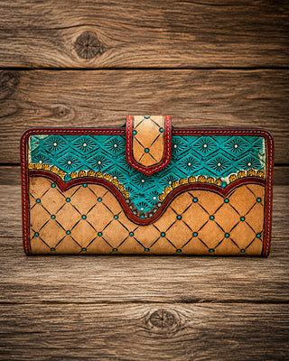 A handcrafted long wallet made of tan leather with turquoise blue geometric patterns, red stitching, and gold accents, displayed on a rustic wooden background.