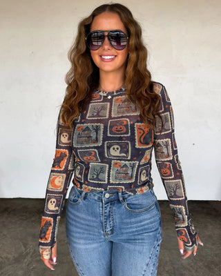 Woman wearing a patterned long-sleeve shirt and jeans with sunglasses indoors.
