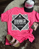 Flat lay featuring neon pink Bronco Western Supply Co. tee with back graphic