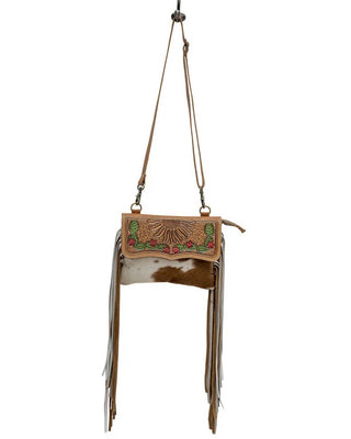 A western-style fringe crossbody bag with a tan leather flap featuring a sunburst tooling design and colorful beadwork, a brown and white cowhide body, and long tan leather fringe, shown against a plain white background.