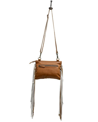 A brown leather crossbody bag with long white fringe hanging from the bottom, shown hanging against a plain white background.