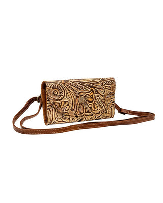 A brown leather crossbody clutch bag with intricate hand-tooled floral and scroll patterns on the front flap, shown against a plain white background.