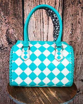 A turquoise and white checkered leather handbag with double top handles, displayed on a round wooden stool against a rustic wood plank background.