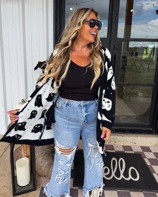 Woman wearing a black and white patterned cardigan, black top, and ripped jeans standing on a porch.