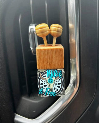 Car air freshener with wooden design and 'Wild & Free' text in a car's air vent.