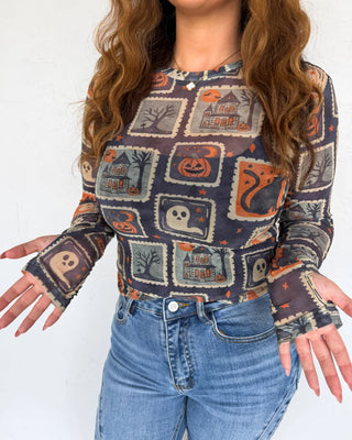 Person wearing a Halloween-themed long-sleeve shirt with pumpkins, ghosts, and cats on a white background.