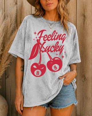 Woman wearing a gray t-shirt with red graphic design and text, standing against a wooden wall.