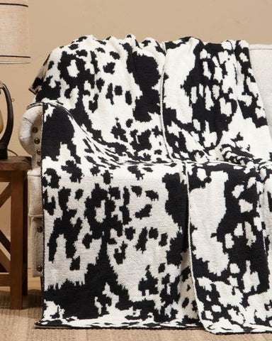 Black and white patterned blanket draped over a chair in a room with a lamp and small table.