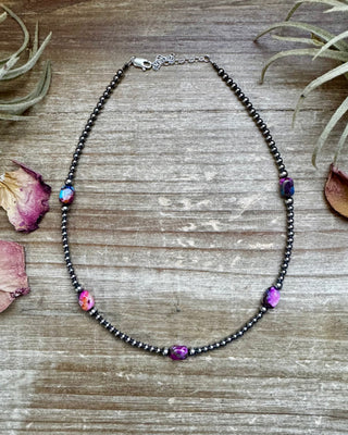 Necklace with colorful beads on a wooden surface with dried leaves and plants.