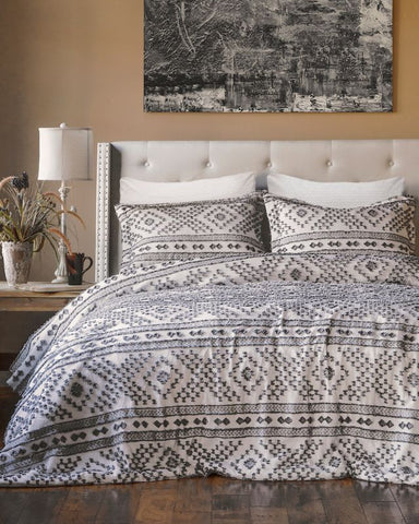 Bedroom with patterned bedding, pillows, and a lamp on a nightstand.