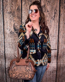 Woman holding a brown handbag with intricate designs against a wooden background