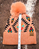 The Aztec Pom Beanie, shown on a cowhide backdrop with a ruler indicating it measures about 8 inches tall.
