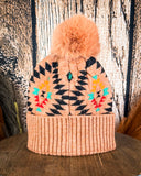 The Aztec Pom Beanie displayed on a wooden table with a wood background.