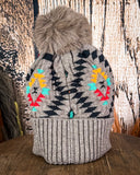 The Aztec Pom Beanie displayed on a wooden table with a wood back ground.