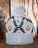 The Aztec Pom Beanie displayed on a wood table with a wood background.