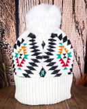 The  Aztec Pom Beanie displayed on a wooden table with a wood background.