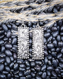 Silver earrings on black beans with wheat.