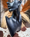 Black mannequin bust with decorative earrings on a rustic background